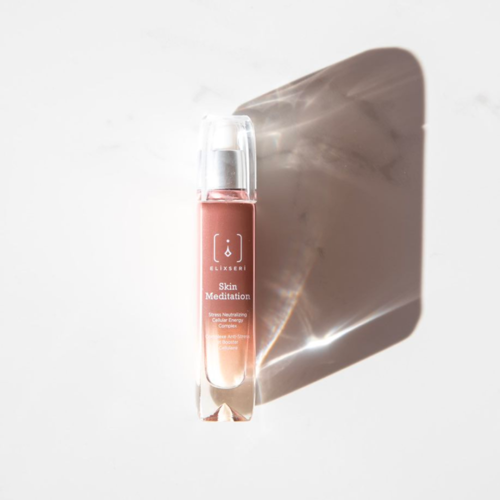 Eine rosa-braune Glasflasche mit dem Serum Elixseri Skin Meditation auf einem weißen Marmorhintergrund mit einem Schatten.