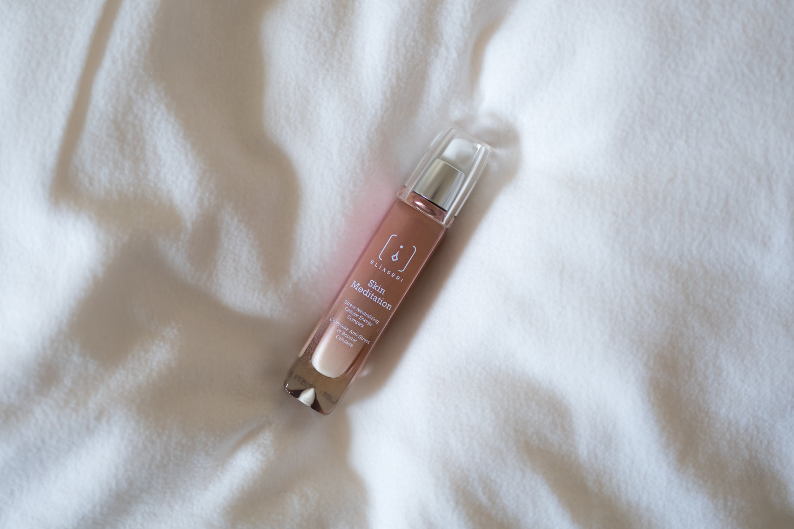 A browny pink bottle of Elixseri Skin Meditation on a soft white pillow
