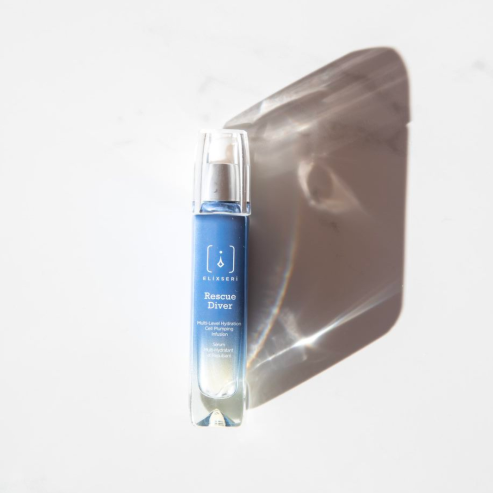 A blue glass bottle of Elixseri Rescue Diver serum on a white marble background with a shadow