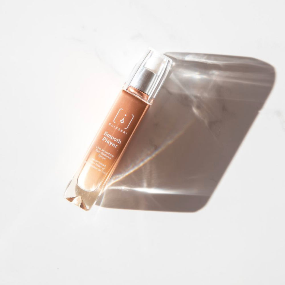 An orange glass bottle of Elixseri Smooth Player serum on a white marble background with a shadow.