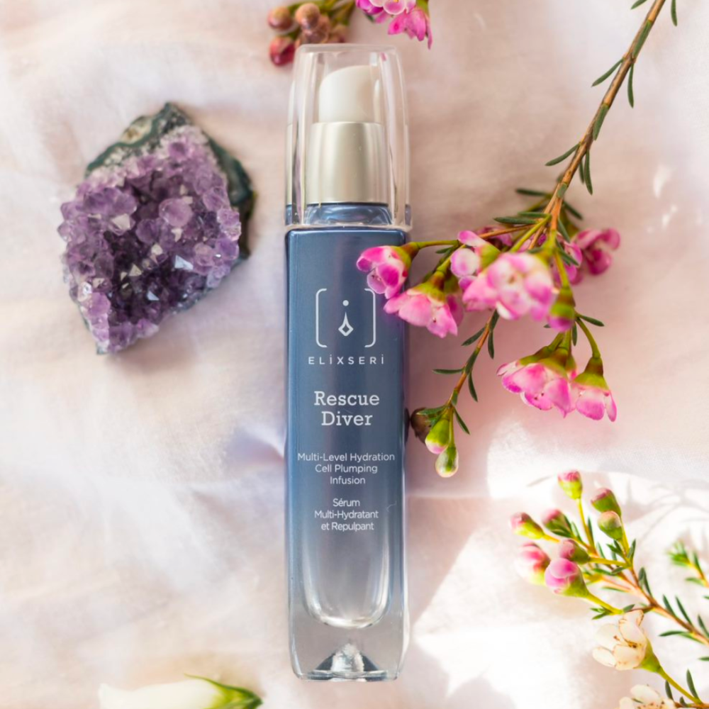 A blue bottle of Elixseri Rescue Diver serum amongst flowers and crystals.