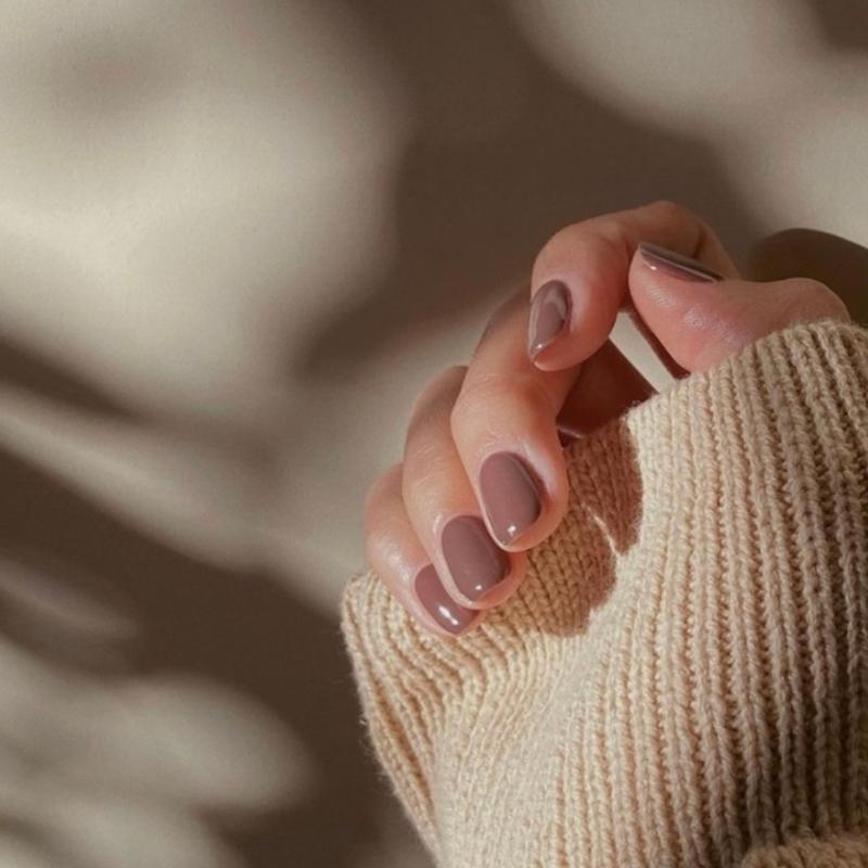 A womans hand with painted beige nails in a wooly jumper sleeve
