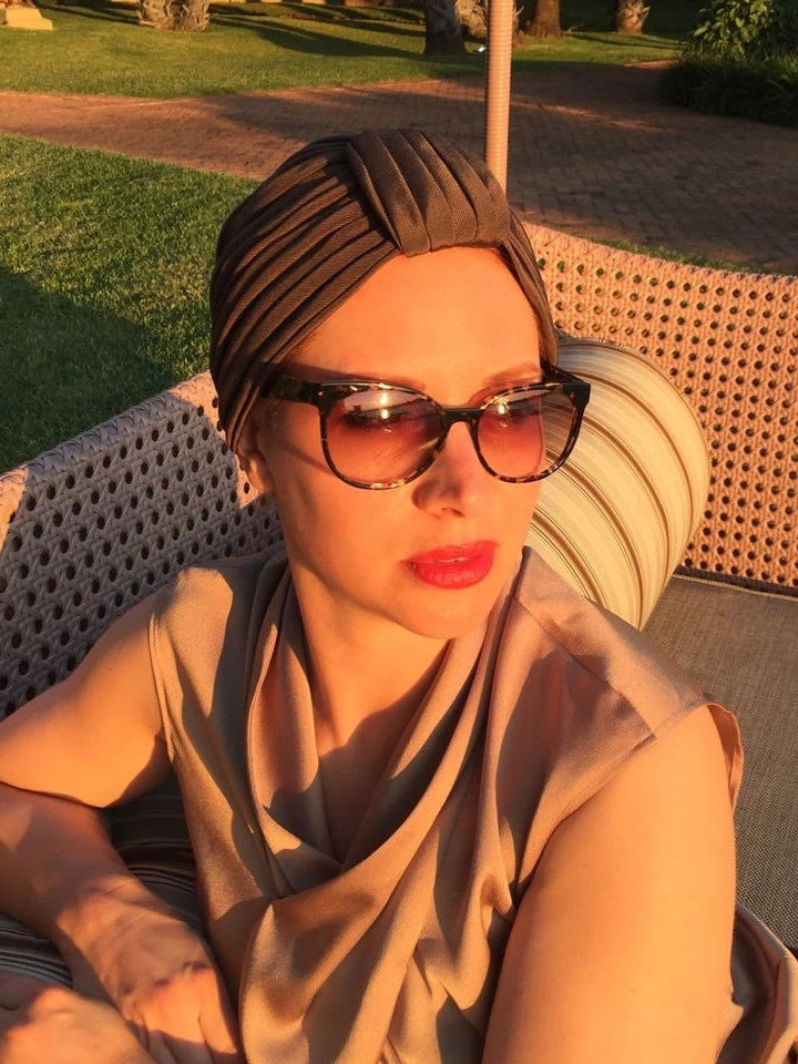 A woman glowing in evening sunlight wearing sunglasses and a chic silk turban
