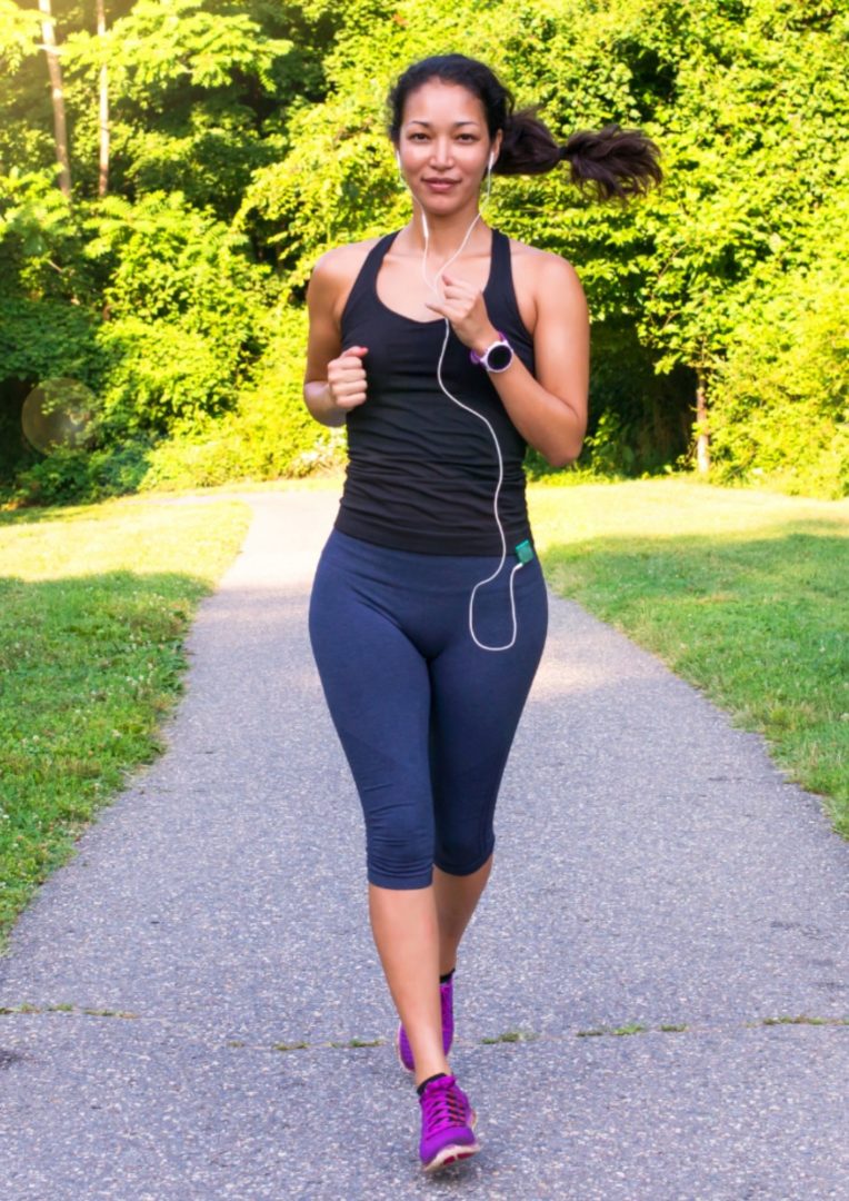 A woman running towards the camera with headphones on. 