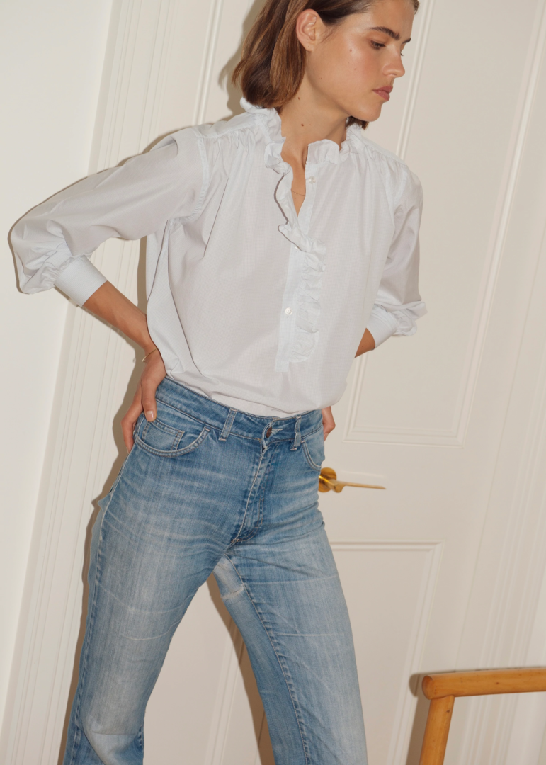 Model with dark blonde hair wearing blue denim jeans and a white signature Alma shirt. 