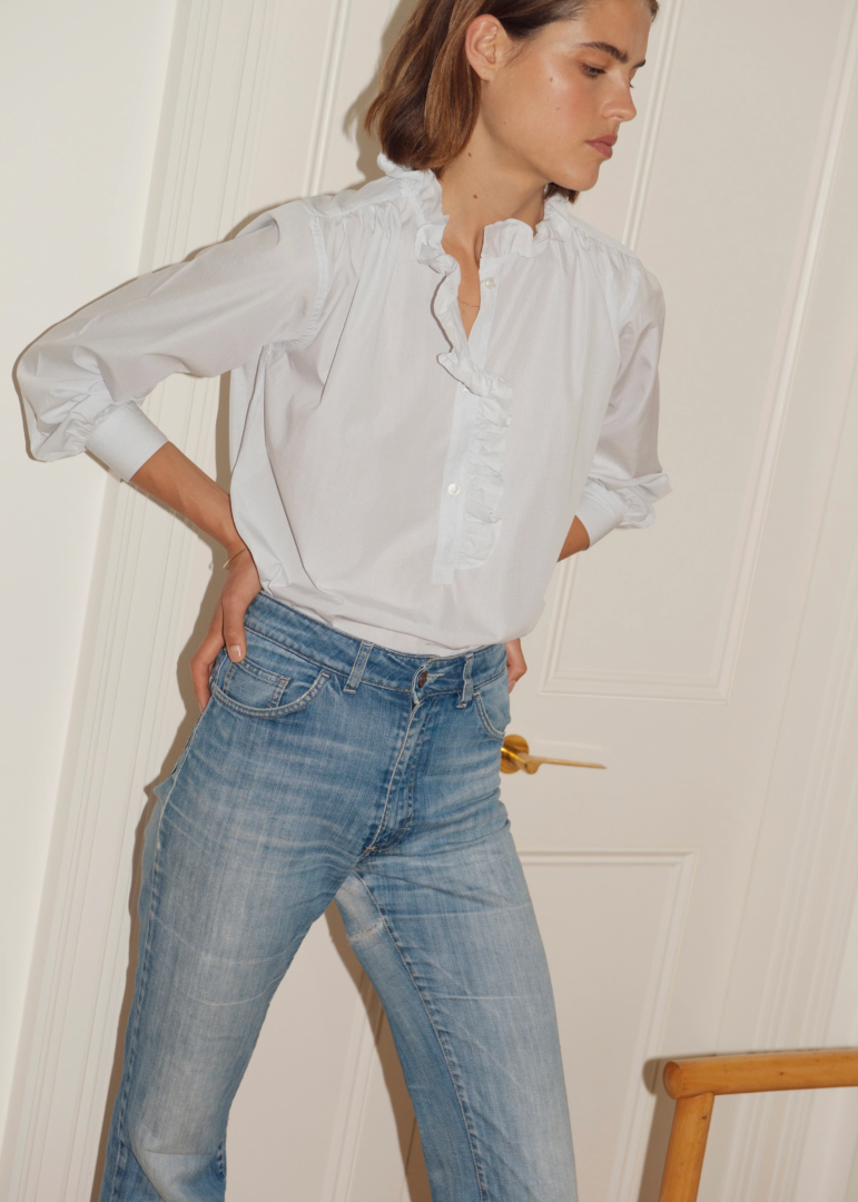 Mannequin aux cheveux blonds foncés portant un jean bleu en denim et une chemise blanche signée Aime. 