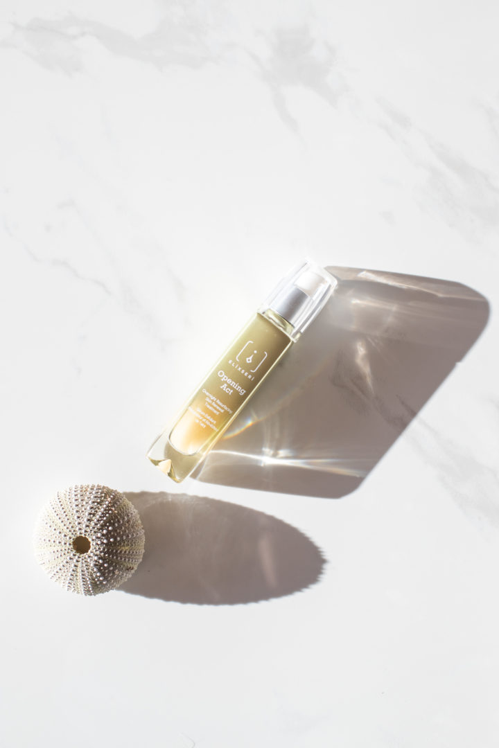 Elixseri's Opening Act serum pictured next to a white shell in summer sun. 