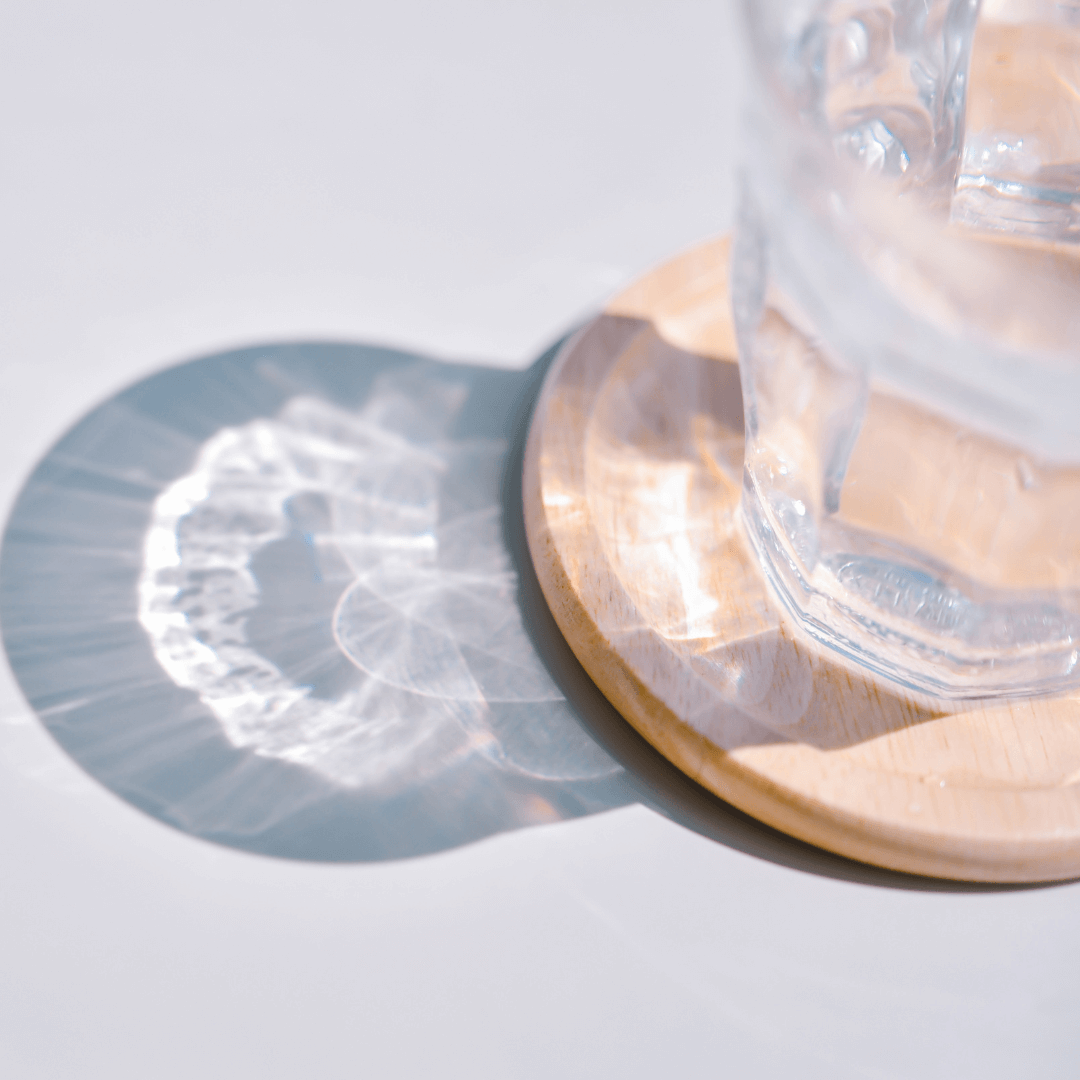 A glass of water on a wooden coaster with sun shining through it