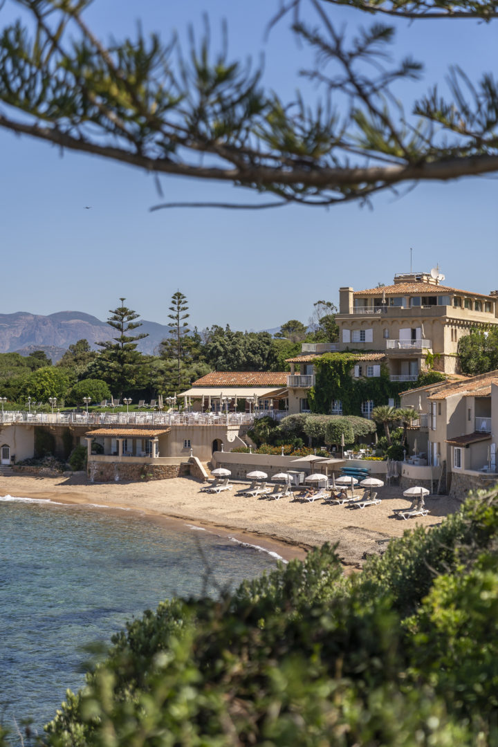 Blick auf den Strand von Korsika im Hotel Maquis mit weißen Sonnenschirmen, die auf dem Sand aufgereiht sind
