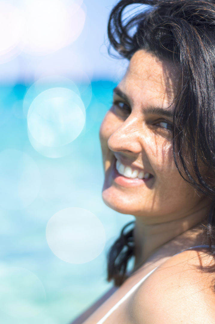 Une femme sourit à l'appareil photo par-dessus son épaule, sous le soleil.