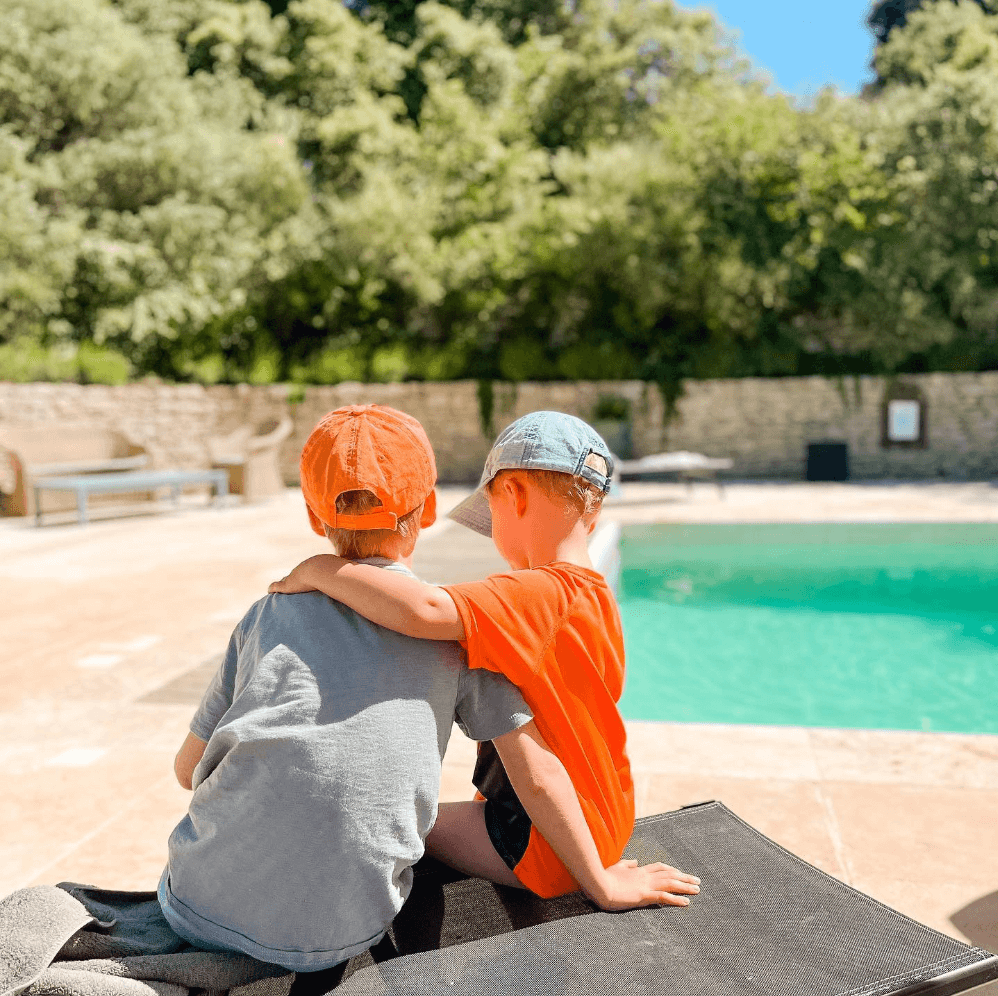 Die Kinder von Sadie Reid sitzen mit dem Rücken zur Kamera vor einem Swimmingpool und halten sich gegenseitig in den Armen.