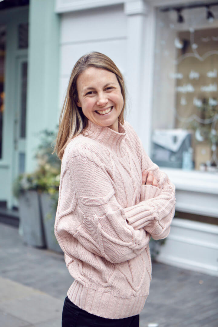 Sadie Reid, Gründerin der Zeitschrift Hip & Healthy, lächelt mit verschränkten Armen in die Kamera und trägt einen rosa Pullover.