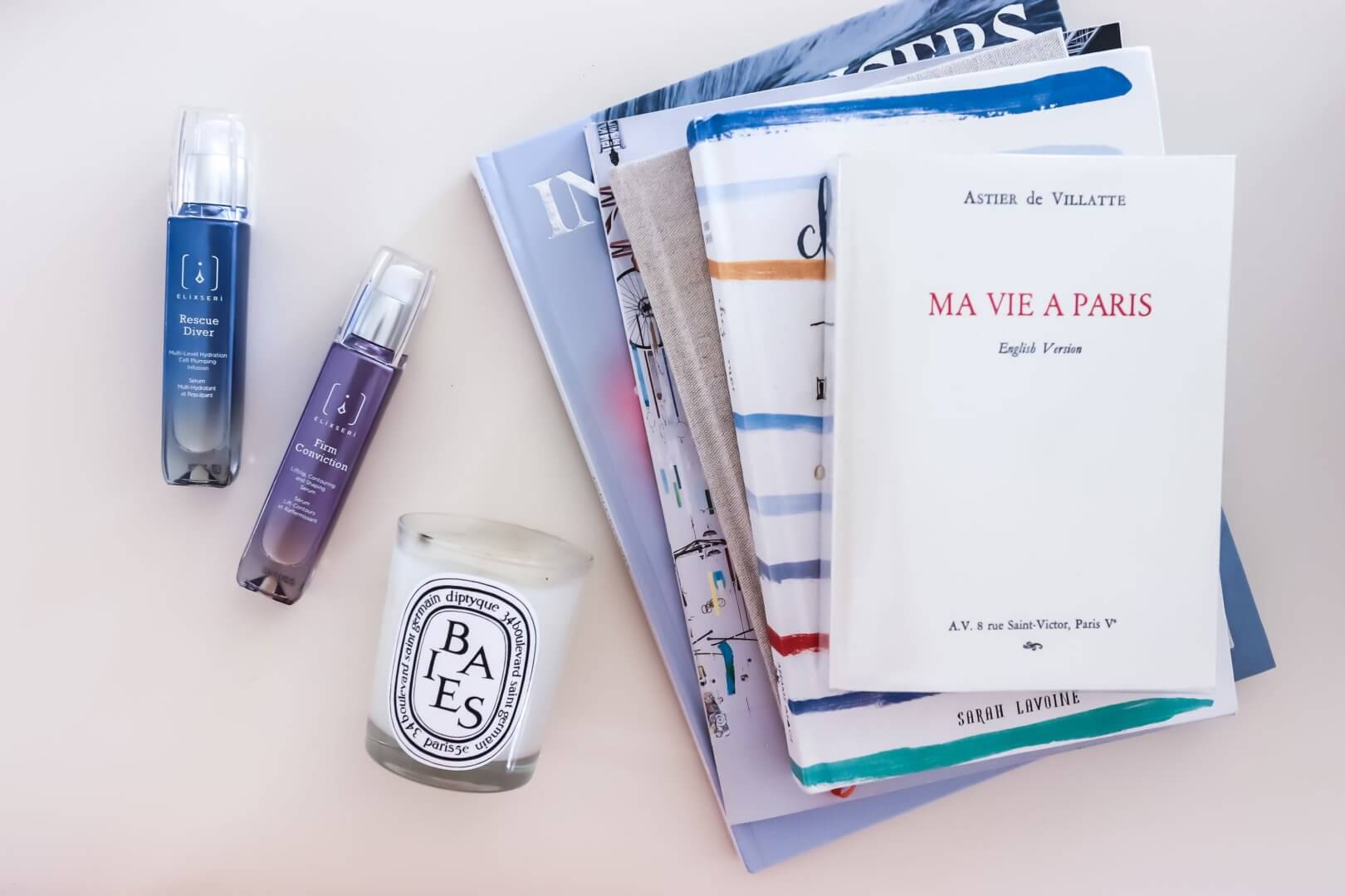 Elixseri Rescue Diver and Firm Conviction serums pictured next to a Diptyque Baies candle and a selection of books.