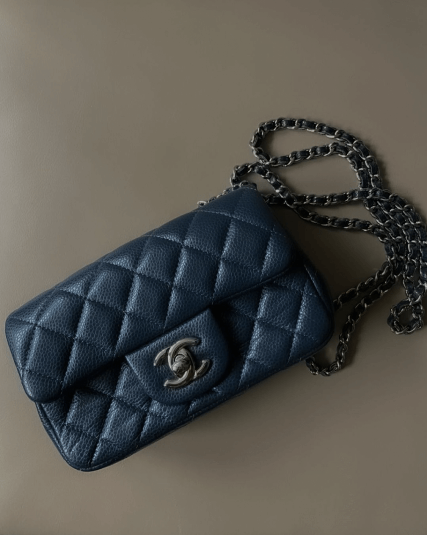 Eine marineblaue gesteppte Chanel XL-Handtasche aus Leder auf beigem Hintergrund.