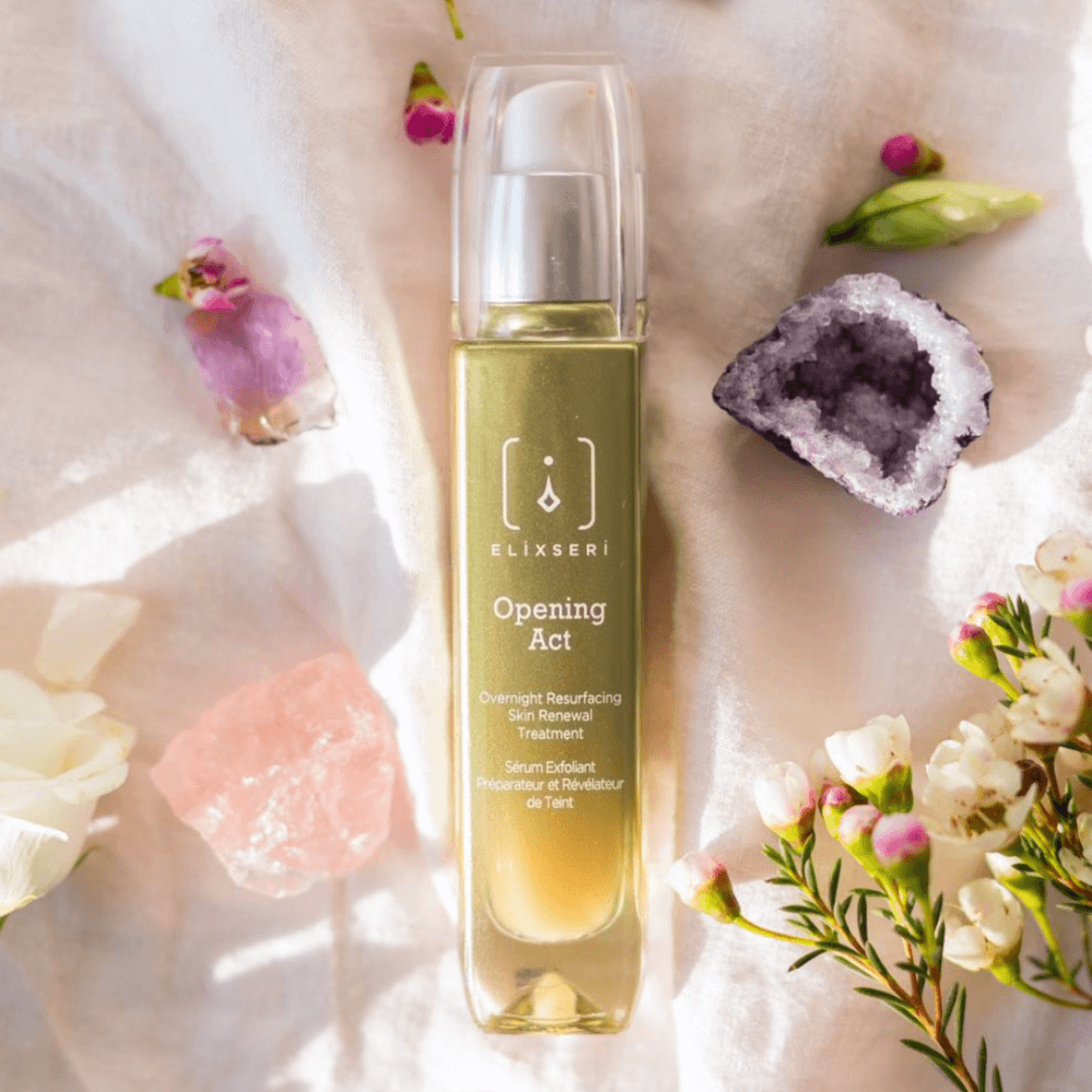 A green bottle of Elixseri Opening Act serum amongst flowers and crystals.