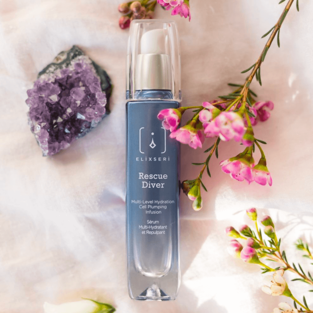 A blue bottle of Elixseri Rescue Diver serum amongst flowers and crystals.