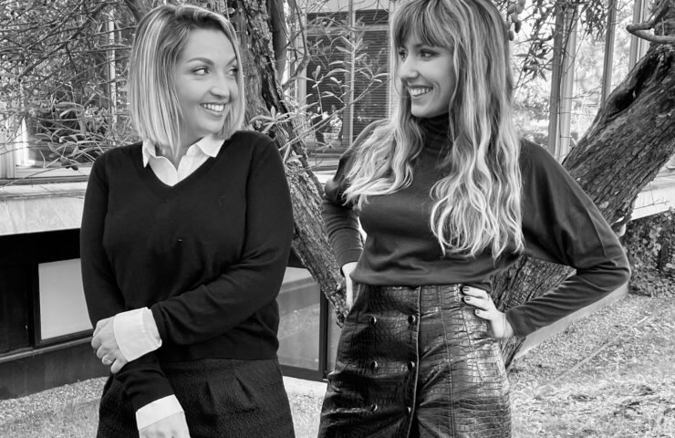 A black & white photo of two French ladies smiling wearing smart clothes.