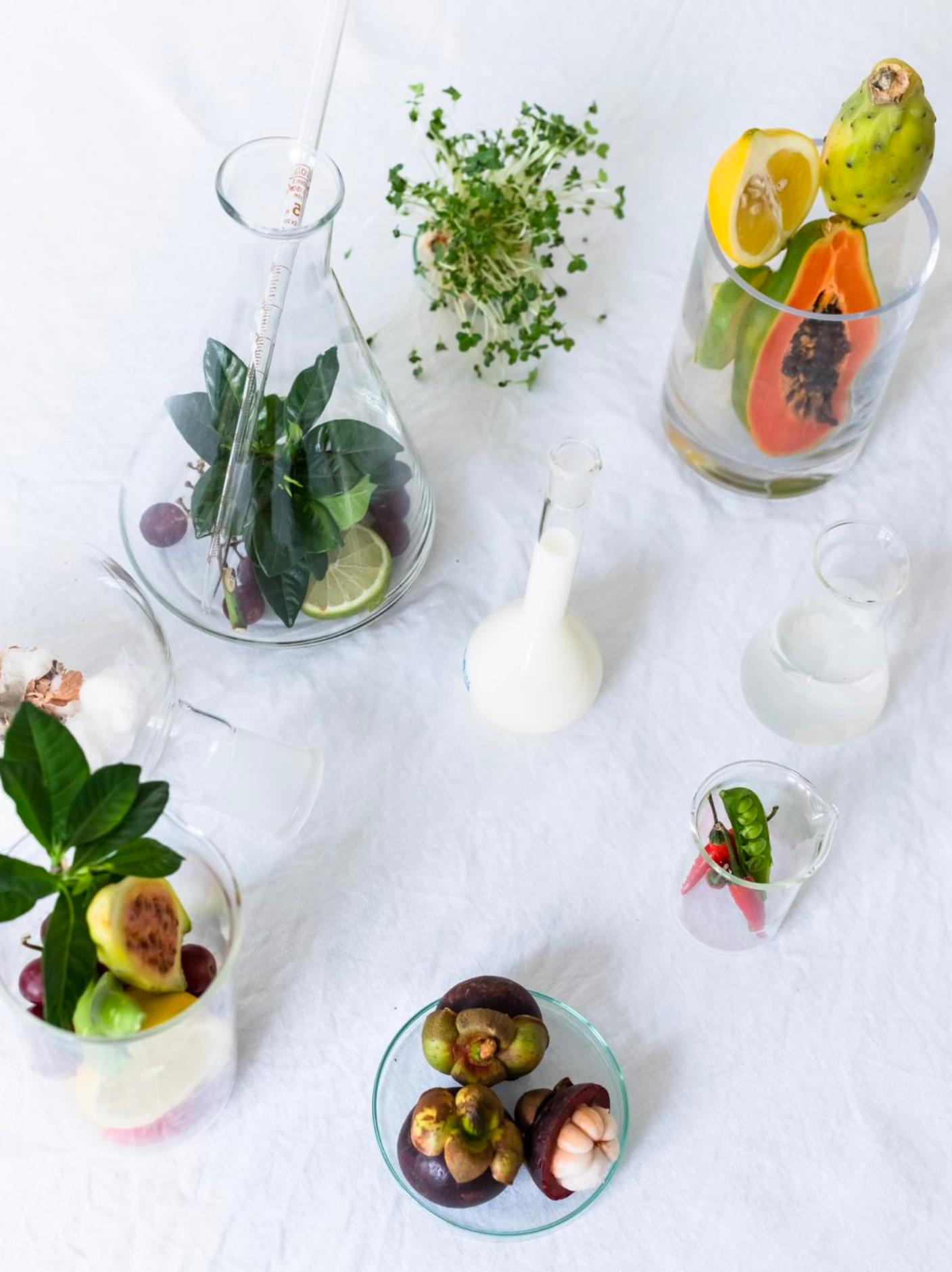 Skincare ingredients pictured in glass science beakers on a white cloth background.