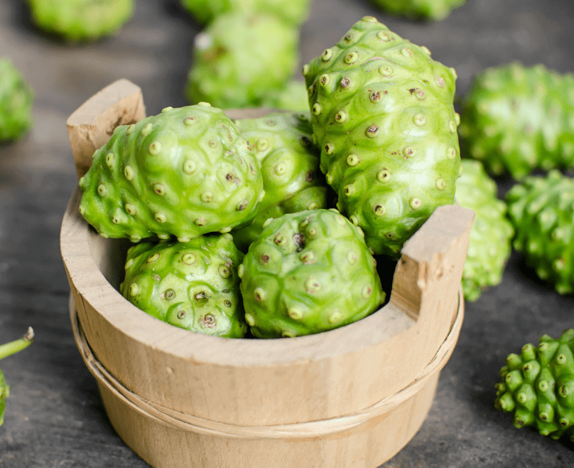 A wooden bucket of green Noni fruit