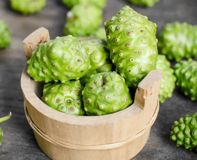 Un seau en bois plein de fruits verts Noni
