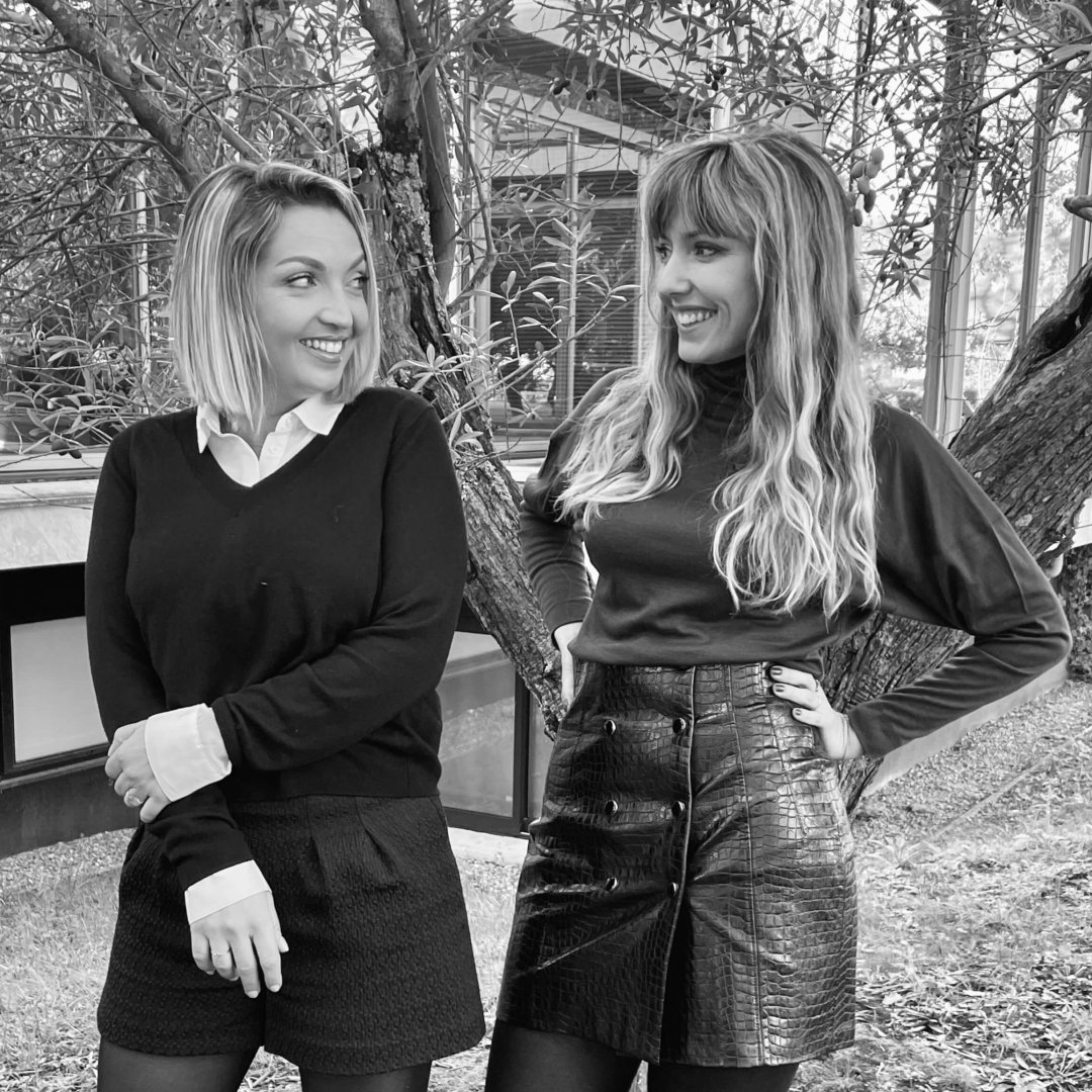A black & white photo of two French ladies smiling wearing smart clothes.